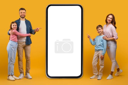 Foto de Una familia feliz de cuatro personas se levanta contra un fondo amarillo brillante, con los padres y sus dos hijos apuntando alegremente a una gran pantalla de teléfono inteligente en blanco a su izquierda - Imagen libre de derechos