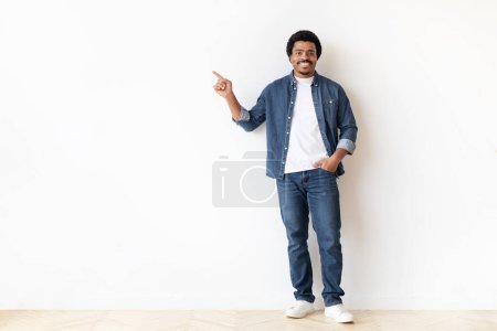 Foto de Hombre afroamericano de pie contra una pared blanca, mirando hacia adelante con una expresión neutral. La pared proporciona un telón de fondo marcado, haciendo hincapié en la presencia de los hombres en el espacio. - Imagen libre de derechos