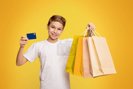 Foto de Muchacho alegre mostrando sus bolsas de la compra y tarjeta de crédito o débito, fondo naranja - Imagen libre de derechos