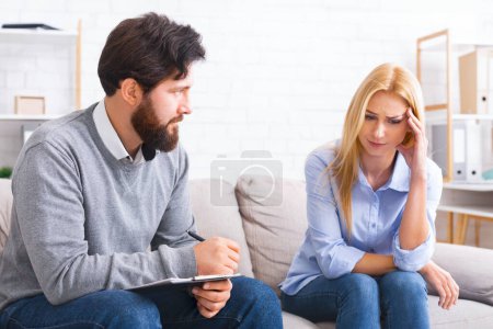 A seated man, possibly a counselor or therapist, is attentively listening to a woman who appears distressed or concerned.