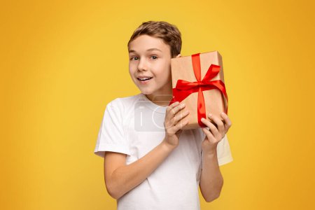 A boy, young in age, holding a wrapped present box in his hands, expressing excitement and anticipation.