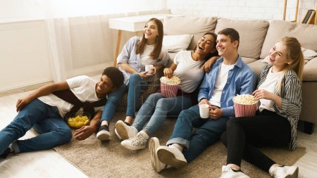 Photo for Several friends sitting on the floor together, each holding a bag of popcorn and eating. The group appears relaxed and engaged in conversation as they enjoy their snacks. - Royalty Free Image
