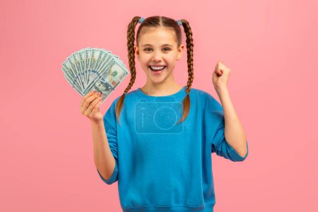 A young girl is seen holding a fan of money in her hand. She looks curious and excited as she grips the bills tightly.