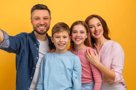 Un homme est debout avec sa famille, capturant un selfie avec un smartphone. Ils sourient et posent ensemble pour l'autoportrait.