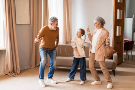 An elderly couple is joyfully dancing with a young child in the warmth of a well-lit living room. The trio appears to be having a delightful time, sharing smiles and an apparent love for music