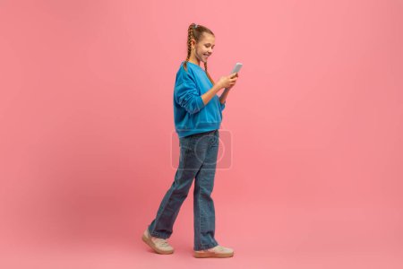 Téléchargez les photos : Une jeune fille portant une chemise bleue se concentre sur son écran de téléphone portable dans ce moment franc capturé dans un cadre public. Elle semble absorbée par son téléphone, peut-être par des messages ou des défilements - en image libre de droit