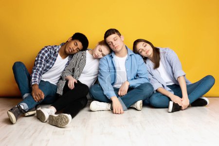 Eine bunt gemischte Gruppe multiethnischer Teenager sitzt eng auf dem Boden, lehnt sich mit geschlossenen Augen aneinander und signalisiert Müdigkeit oder Trost miteinander