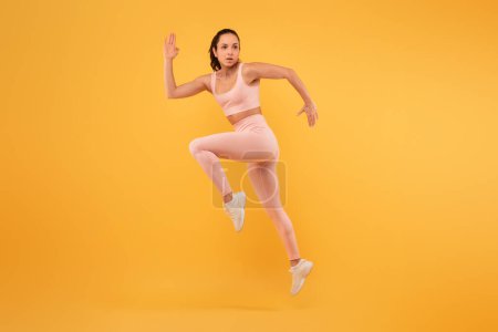 Eine Frau im rosafarbenen Outfit wird in der Luft gefangen genommen, während sie energisch springt. Ihre Arme sind ausgestreckt und ihre Beine gebeugt, was einen Moment dynamischer Bewegung und Freude darstellt..