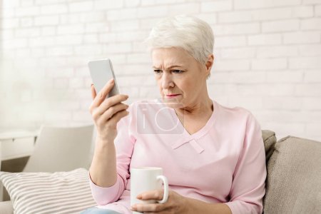 Téléchargez les photos : Myopie. Femme âgée tenant le téléphone près du visage, essayant de voir le message, espace libre - en image libre de droit