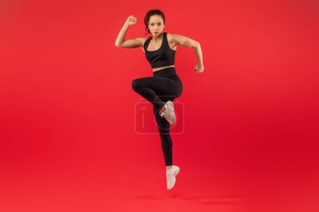 Eine Fitnesstrainerin wird während einer Übung mit hohen Knien in der Mitte der Bewegung gefangen genommen und stellt ihre Kraft und Beweglichkeit unter Beweis. Sie ist athletisch gekleidet und wirkt konzentriert und entschlossen