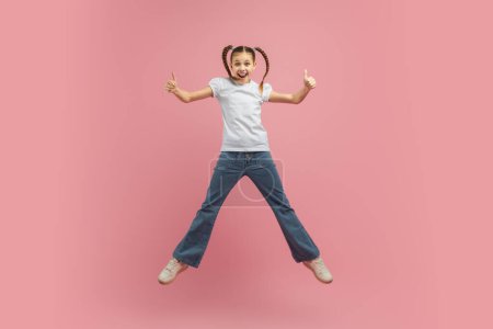 A young girl child is joyfully leaping into the air with her arms outstretched. She appears to be full of energy and excitement as she jumps high off the ground.