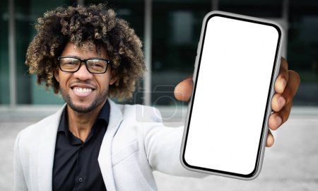 Téléchargez les photos : Homme noir debout et tenant un smartphone devant lui, affichant un écran blanc vierge. La main des hommes est clairement visible alors qu'il tient l'appareil droit. - en image libre de droit