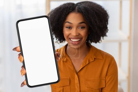 Téléchargez les photos : Femme noire tient un téléphone portable devant elle, l'écran ne montrant rien d'autre qu'une blancheur, l'intérieur du bureau - en image libre de droit