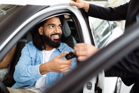Foto de Un hombre indio alegre está sentado dentro de un coche, recibiendo un juego de llaves de un vendedor, lo que sugiere que posiblemente ha hecho una compra o está tomando una prueba de manejo - Imagen libre de derechos