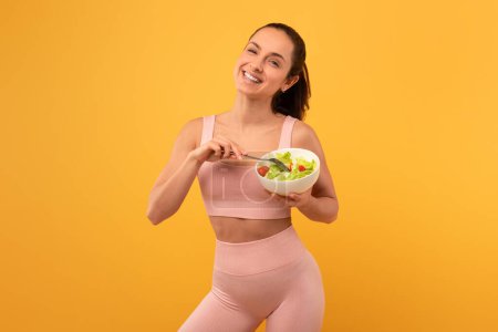 Photo for A woman wearing a pink sports bra top holds a bowl of salad in her hands. She appears healthy and active, showcasing her fitness lifestyle. - Royalty Free Image