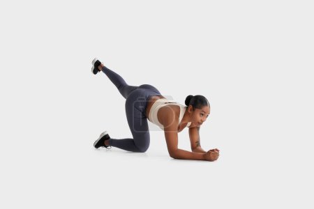 African American woman is seen exercising on a plain white background. She is engaged in physical activity, demonstrating strength and flexibility through various poses and movements.