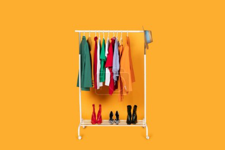 Téléchargez les photos : Une étagère remplie de divers vêtements est affichée sur un fond jaune vif. Les vêtements sont soigneusement accrochés et disposés, présentant différents styles et couleurs prêts pour les clients - en image libre de droit