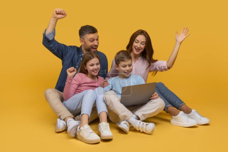 Foto de Una familia alegre que consiste en un padre, una madre y dos hijos están sentados junto con una computadora portátil, expresando emoción y felicidad con los puños levantados y sonrisas anchas - Imagen libre de derechos
