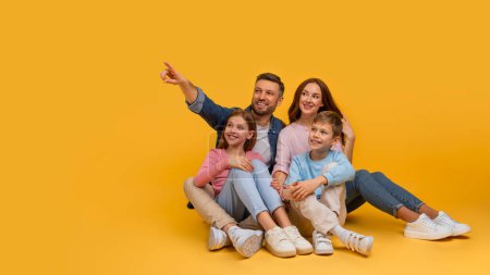 A joyful family is sitting closely with a father pointing at something out of frame, creating a moment of togetherness and curiosity, pointing at copy space on yellow background