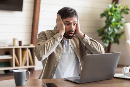 Ein Mann sitzt konzentriert vor einem Laptop und hält frustriert oder nachdenklich den Kopf. Er scheint tief in Gedanken zu sein oder eine Art psychische Belastung zu empfinden.