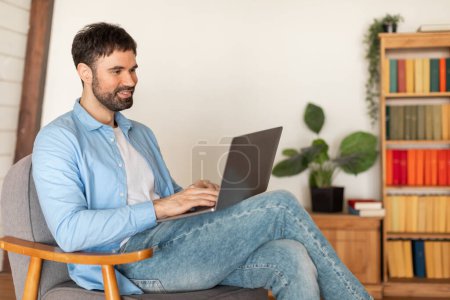 Ein Mann sitzt auf einem Stuhl, konzentriert auf einem Laptop-Computerbildschirm. Seine Hände tippen auf der Tastatur, während er arbeitet. Der Raum wirkt hell, Kopierraum