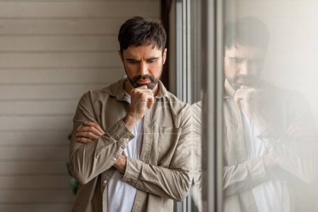 A contemplative man leaning on a large window pane, with his reflection visible. He appears deep in thought, resting his chin on his hand. His expression is one of serious contemplation or concern