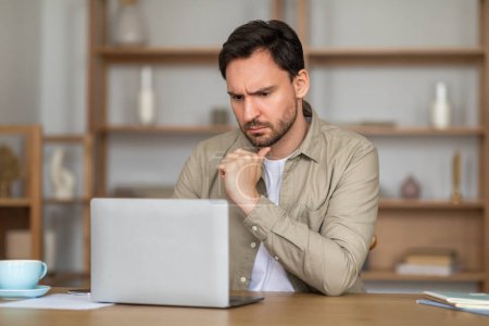 Un hombre aparece profundamente en el pensamiento mientras trabaja en una computadora portátil colocada en una mesa de madera. Su lenguaje corporal emana concentración y posiblemente cierta preocupación, ya que apoya su barbilla en su mano.