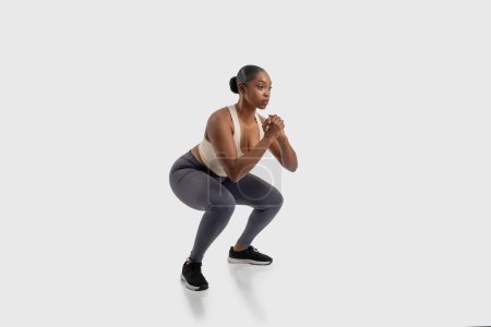 A focused African American woman athlete is engaged in a strength-building exercise routine, demonstrating perfect form while doing squats on white background