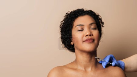 Eine Frau wird dargestellt, wie sie eine Spritze in den Hals bekommt. Der medizinische Eingriff wird von einem medizinischen Fachpersonal in einem klinischen Umfeld durchgeführt..