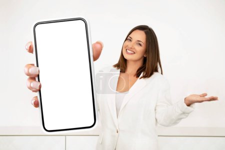 Téléchargez les photos : Une femme entrepreneure est montrée tenant un téléphone portable dans sa main, regardant l'écran. Elle semble concentrée sur l'appareil, l'autre main détendue à ses côtés. - en image libre de droit