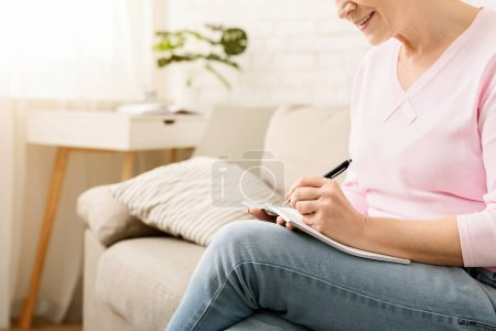 Eine Frau sitzt auf einer Couch und konzentriert auf ein Blatt Papier. Sie scheint mit dem Stift in der Hand und einem konzentrierten Blick auf ihr Gesicht bei der Aufgabe dabei zu sein..