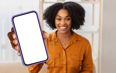 Foto de Mujer afroamericana sostiene un teléfono celular con una pantalla en blanco en la mano, interior de la oficina, maqueta, espacio para copiar - Imagen libre de derechos