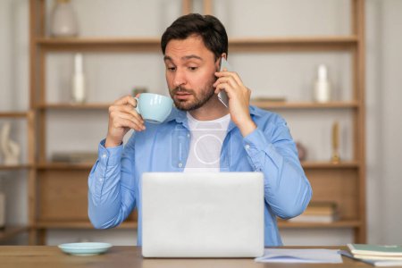 Un hombre está de pie con una taza de café en la mano, participando en una conversación en su teléfono. Parece concentrado en la llamada mientras sostiene el teléfono al oído..