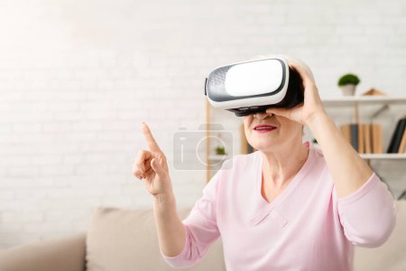 Mujer mayor con una camisa rosa se centra en el uso de un dispositivo virtual. Ella está interactuando con la pantalla, presumiblemente comprometida en una tarea o actividad digital, primer plano, espacio de copia