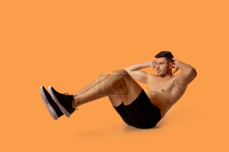 Un jeune homme en forme fait des croque-vélo sur un fond orange solide dans un studio, mettant en valeur sa force et sa routine de remise en forme.