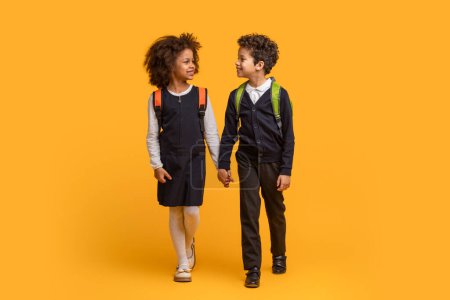 Zwei afroamerikanische Kinder in Schuluniformen stehen nebeneinander vor leuchtend gelbem Hintergrund. Beide Studenten scheinen vorausschauend zu sein und posieren möglicherweise für ein schulbezogenes Ereignis