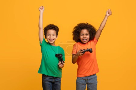Vor orangefarbenem Hintergrund sind zwei afroamerikanische Jungen zu sehen, die jeweils einen Videospielcontroller in der Hand halten. Sie wirken fokussiert und engagiert, wenn sie mit den Kontrolleuren interagieren.