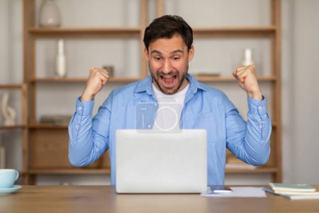 Téléchargez les photos : A man is energetically celebrating in front of a table while holding a laptop. He appears to be excited and joyful, possibly achieving a goal or receiving good news. - en image libre de droit
