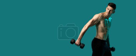 A man is lifting dumbbells while standing on a green background. He is focused and determined, with his muscles engaged. The mans form is precise as he performs the exercise, empty space
