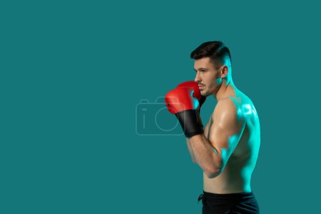 A man wearing boxing gloves strikes a dynamic pose on a vibrant green background. His stance exudes strength and determination as he showcases his boxing skills, copy space