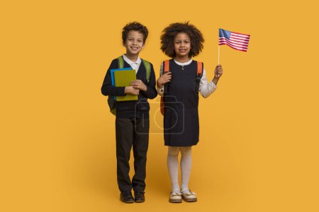 Afroamerikanische Jungen und Mädchen in Schuluniformen stehen mit strahlendem Lächeln nebeneinander, halten einen Stapel bunter Notizbücher in der Hand und schwenken stolz eine kleine amerikanische Flagge.