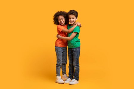 Zwei afroamerikanische Kinder umarmen sich herzlich auf einem leuchtend gelben Hintergrund. Ihre Arme sind in einer liebevollen Umarmung umschlungen.