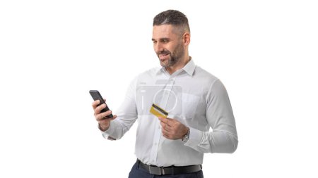 A businessman dressed in a white shirt, holding a credit card in one hand and using a smartphone with the other. He appears to be engaging in an online transaction or checking account details.