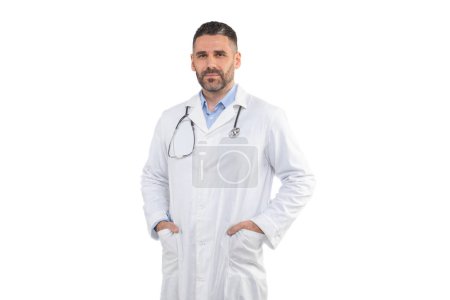 Un médico hombre está de pie con las manos en los bolsillos, con una bata de laboratorio blanca y estetoscopio, sobre un fondo blanco liso. Se ve profesional y listo para ayudar a los pacientes.
