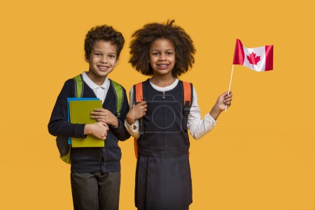 Afroamerikanische Jungen und Mädchen, beide in Schulrucksäcken und lässiger Kleidung, stehen Seite an Seite mit strahlendem Lächeln. Das Mädchen hält eine kleine kanadische Flagge in der Hand, beide sind mit Notizbüchern ausgestattet.