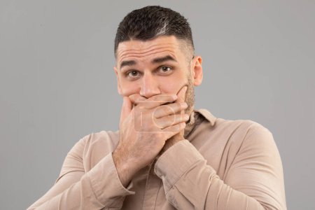 Photo for A man covers his mouth with his hands, possibly to stifle a cough, sneeze, or yawn. His hands are pressed firmly against his lips, indicating a deliberate action. - Royalty Free Image