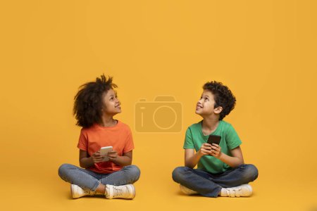 Deux enfants afro-américains s'assoient par terre, absorbés par leurs smartphones. Leur attention se concentre uniquement sur les écrans, car ils interagissent avec le monde numérique autour d'eux, copier l'espace