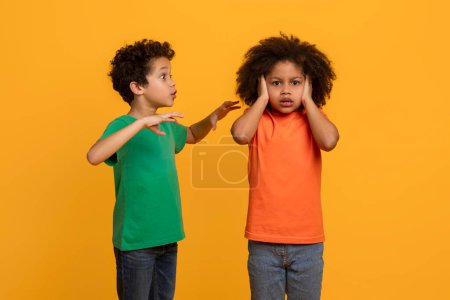 Two African American boys, engaged in a heated argument, are pictured against a bright yellow background. Their expressions are tense and gestures animated as they dispute.