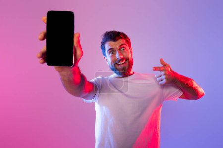 Foto de Un hombre con una camisa blanca está de pie mientras sostiene un teléfono celular en su mano. Parece estar mirando la pantalla del teléfono con una expresión enfocada, maqueta - Imagen libre de derechos