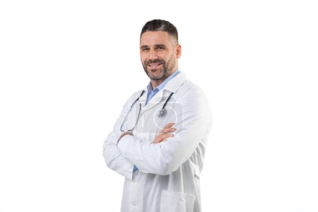 Ein selbstbewusster Arzt steht mit verschränkten Armen in weißem Mantel und Stethoskop vor einem professionellen Studio-Setting und lächelt herzlich. Der weiße Hintergrund